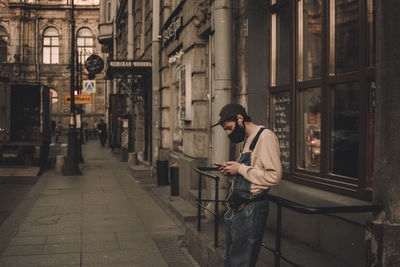 Side view of man using mobile phone by building