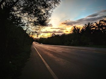 Road by silhouette trees against sky during sunset