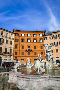 Statue by fountain in city against sky