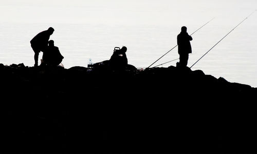 The fascinating silhouette of amateur fishermen on the rocks against the sky