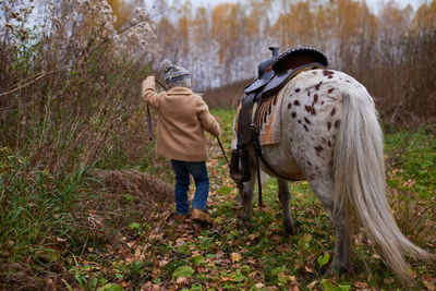 Unrecognizable girl with pony in autumn grove