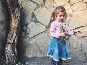 Cute girl holding dandelions while standing against stonewall