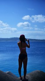 Woman standing on rock looking at sea against sky