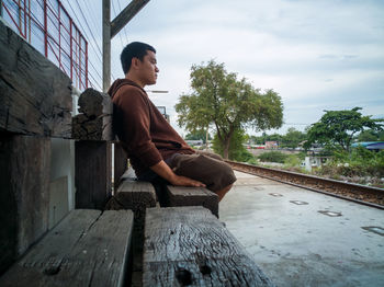 Side view of young man sitting on railroad track