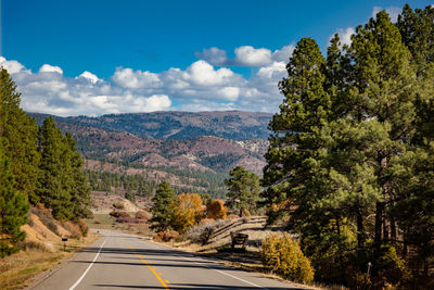 Road amidst trees and mountains against sky