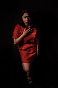 Portrait of woman coughing against black background