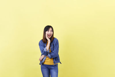 Portrait of young woman standing against yellow background