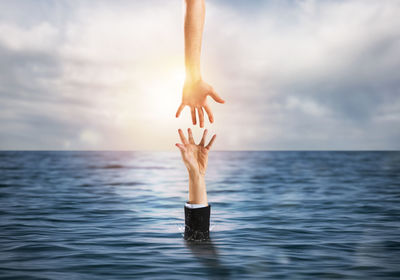 Young woman with arms raised in sea against sky