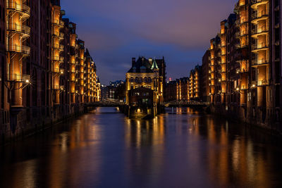 Canal amidst illuminated buildings in city at night