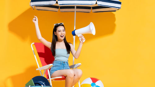 Smiling young woman holding umbrella against yellow wall