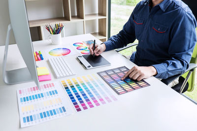 Midsection of creative occupation man using graphics tablet with color swatches on table at office