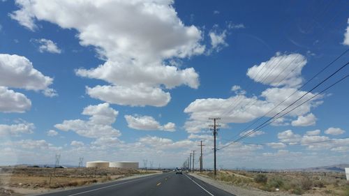 Electricity pylons on road against cloudy sky