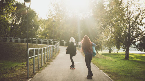 Rear view of women skateboarding on footpath in park