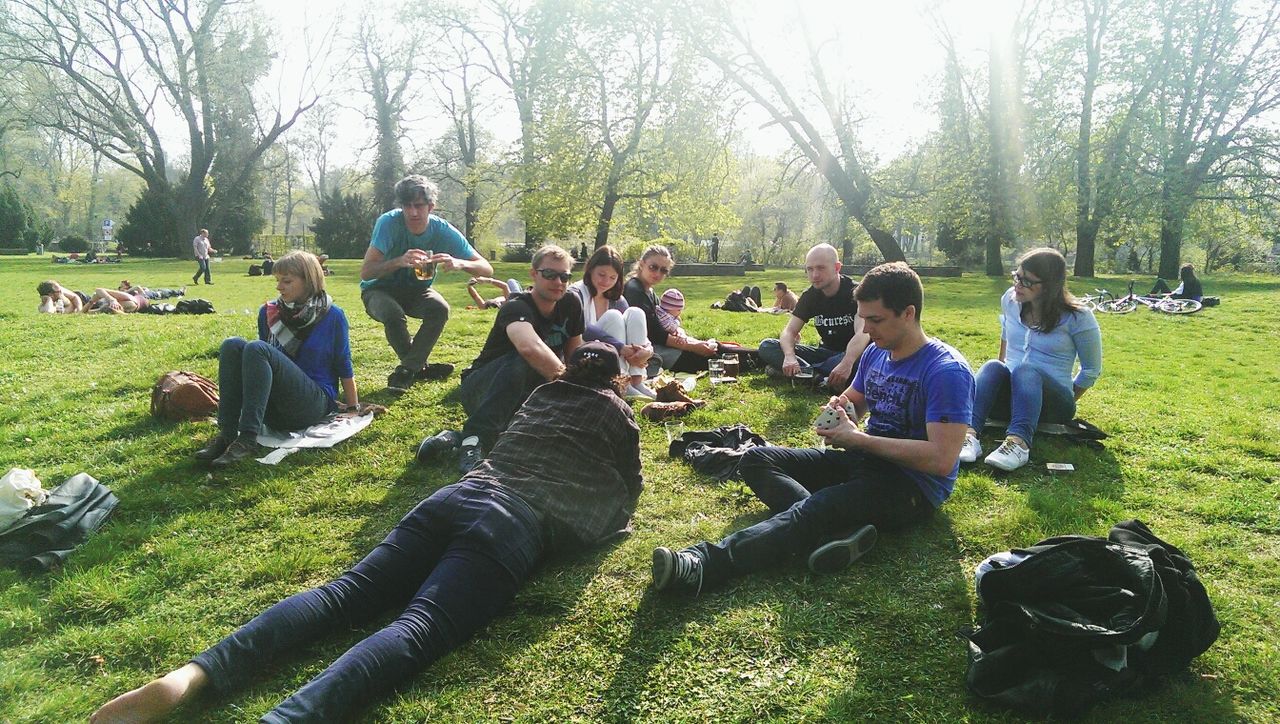 large group of people, tree, grass, men, leisure activity, lifestyles, person, togetherness, park - man made space, sitting, relaxation, green color, park, mixed age range, friendship, enjoyment, medium group of people, field, bonding