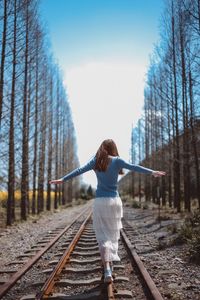 Rear view of woman walking on railroad track against sky