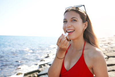 Portrait of smiling young woman applying sun protection on her lip on the beach