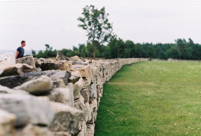 Stone wall by grassy field against sky