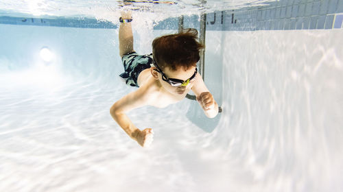 Shirtless cute boy swimming underwater in pool
