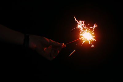 Cropped hand of person holding illuminated sparkler during night