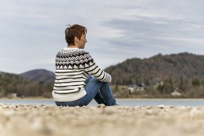 Rear view of woman sitting at lakeshore 