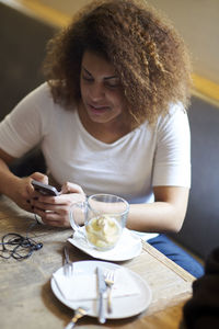 Woman using mobile phone by tea while sitting at restaurant