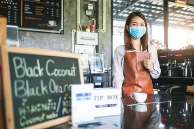Portrait of young woman wearing mask standing at cafe