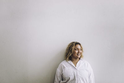 Smiling female fashion designer looking away while standing against wall