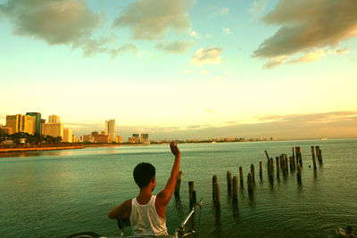 Rear view of boy with bicycle while standing in sea against sky
