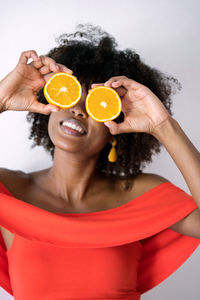 Black woman with afro hair holding cut orange halves in front of her eyes having fun