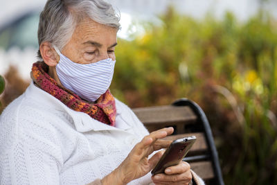 Senior woman wearing mask using smart phone outdoors