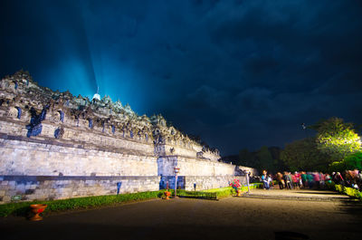 People on illuminated street against sky at night