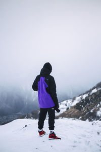 Rear view of boy standing on snow against mountain