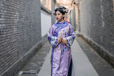 Woman wearing kimono standing on road amidst walls