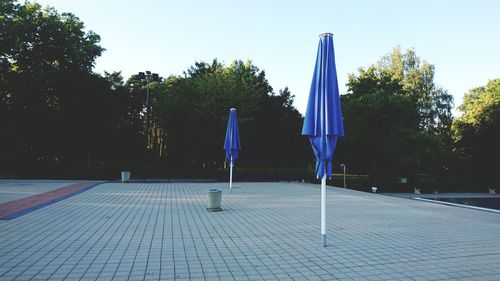 Empty chairs by swimming pool in park against clear blue sky