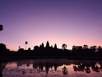 Silhouette plants by lake against sky during sunset