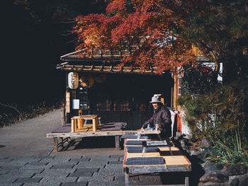 Rear view of man sitting by tree against building