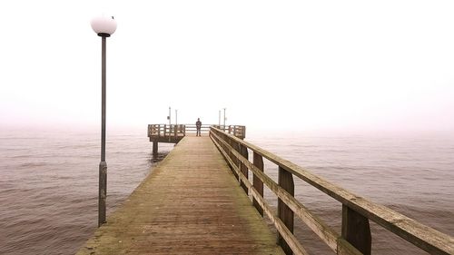 Distance view of man standing on pier over sea against sky