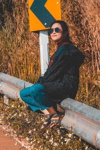 Full length of woman sitting on railing by road
