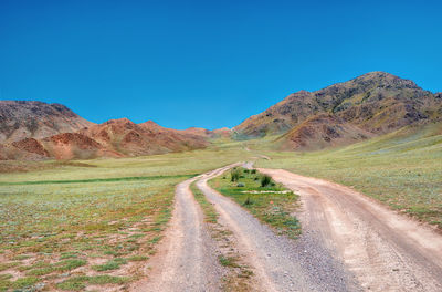 Dirt road amidst landscape against clear blue sky