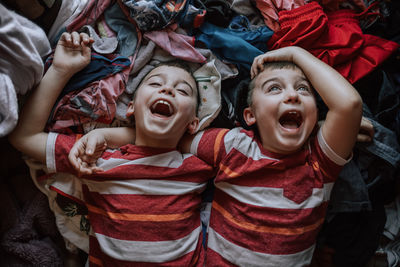 High angle view of laughing boys lying on clothes at home