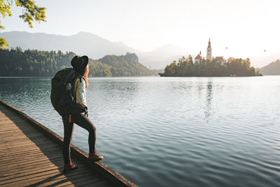 Hipster young woman with backpack enjoying breathtaking  sunrise by the bled lake, slovenia