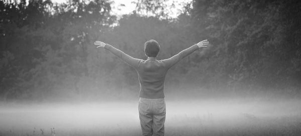 Rear view of woman with arms outstretched standing on land during foggy weather