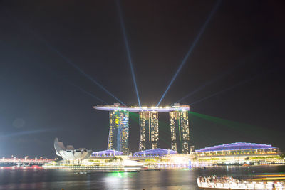 Illuminated city by river against sky at night