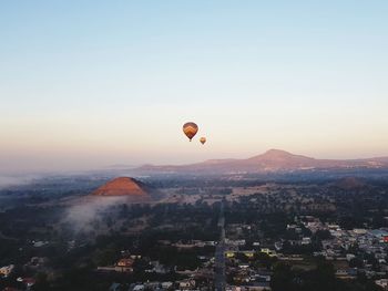 Hot air balloons flying over misty city against sky during sunrise 