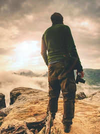 Photographer check weather condition. freelancer stay with camera on cliff and thinking. dreamy fog