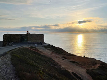 Lighthouse on beach by sea against sky during sunset
