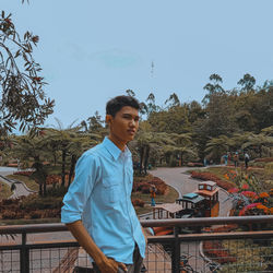 Young man looking away while standing by railing against clear sky