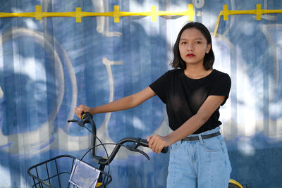 Cute girl holding bicycle standing against wall outdoors