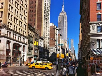 City street by empire state building against clear blue sky