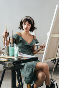 Young woman painting on canvas while sitting on table
